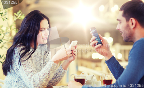 Image of happy couple with smartphones drinking tea at cafe