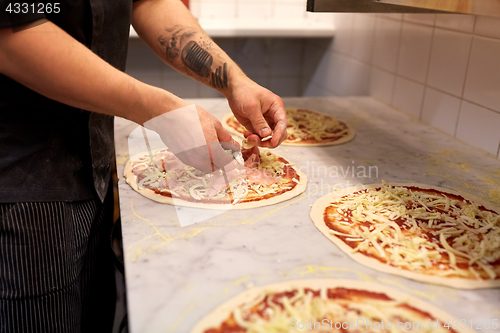 Image of cook hands adding champignons to pizza at pizzeria