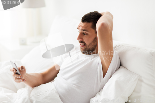 Image of young man with smartphone in bed in morning