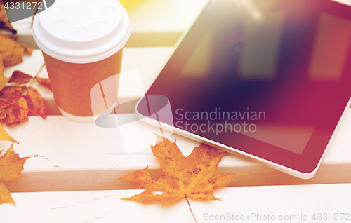 Image of tablet pc and coffee cup on bench in autumn park