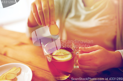 Image of close up of woman adding ginger to tea with lemon