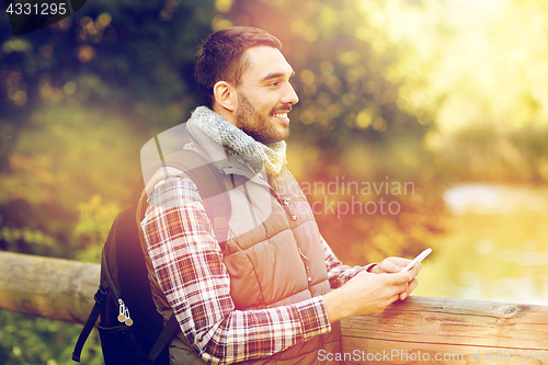 Image of happy man with backpack and smartphone outdoors