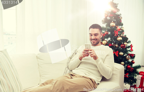 Image of smiling man with smartphone at home for christmas