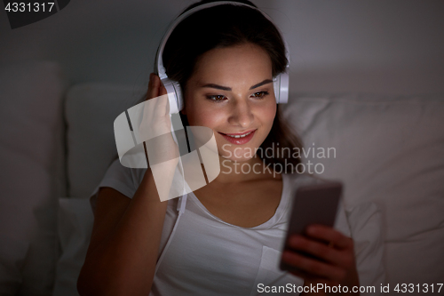 Image of woman with smartphone and headphones in bed