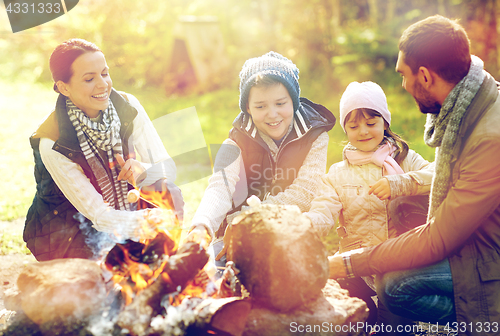 Image of happy family roasting marshmallow over campfire