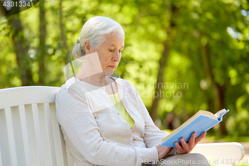 Image of happy senior woman reading book at summer park