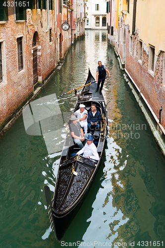Image of Venetian gondolier punting gondola through green canal waters of Venice, Italy