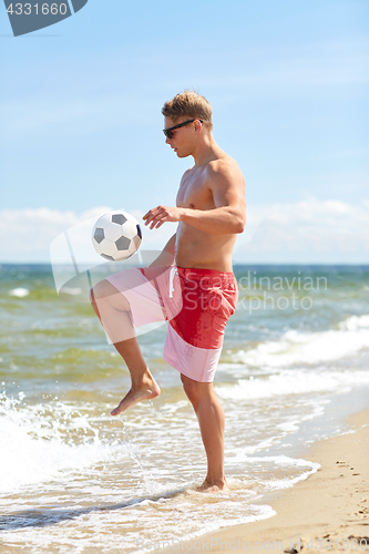 Image of young man with ball playing soccer on beach