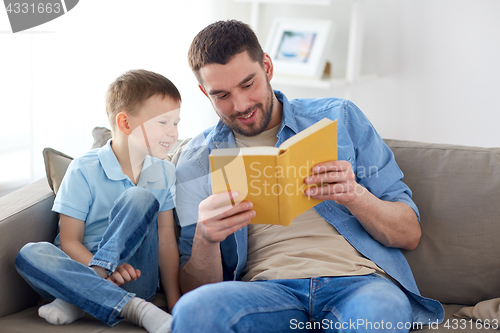 Image of happy father and son reading book sofa at home