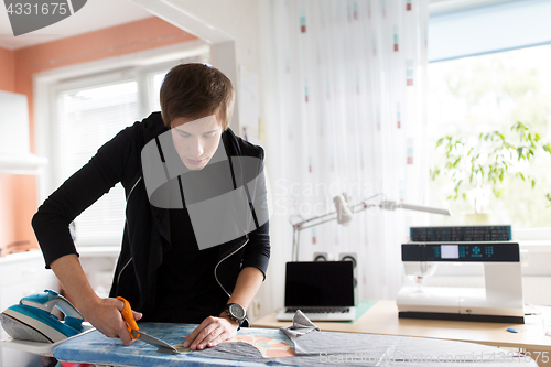 Image of fashion designer cutting fabric at studio