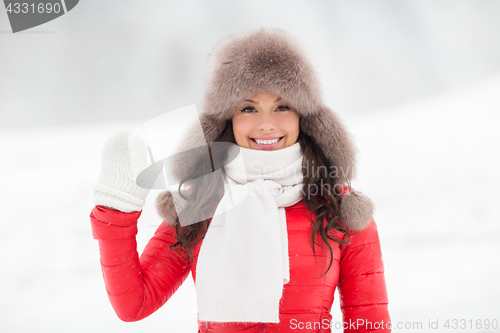 Image of happy woman in winter fur hat waving hand outdoors