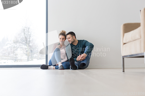 Image of young couple sitting on the floor near window at home
