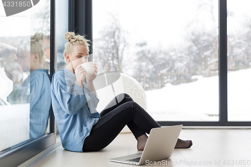 Image of woman drinking coffee and using laptop at home