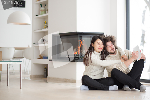 Image of multiethnic couple using tablet computer in front of fireplace