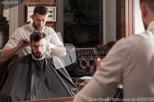 Image of Young handsome barber making haircut of attractive man in barbershop