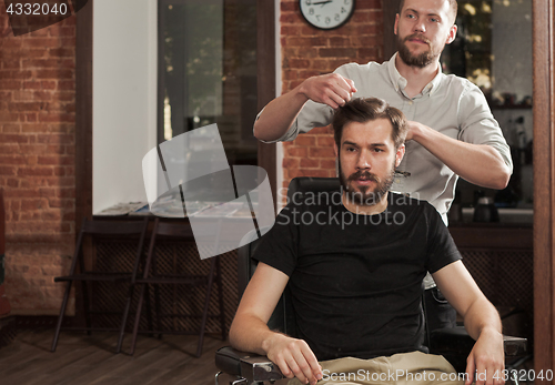 Image of Young handsome barber making haircut of attractive man in barber