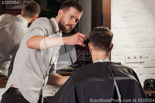 Image of Young handsome barber making haircut of attractive man in barbershop