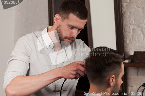 Image of Young handsome barber making haircut of attractive man in barbershop