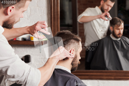 Image of Young handsome barber making haircut of attractive man in barbershop