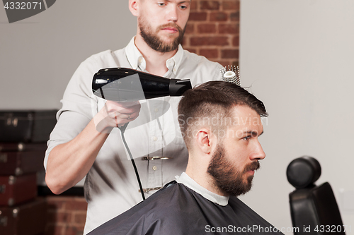 Image of Young handsome barber making haircut of attractive man in barbershop