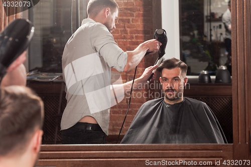 Image of Young handsome barber making haircut of attractive man in barbershop