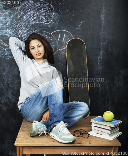 Image of young cute teenage girl in classroom at blackboard seating on table smiling, modern hipster concept, lifestyle people