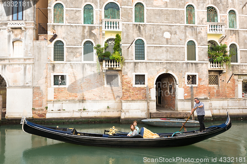 Image of Venetian gondolier punting gondola through green canal waters of Venice, Italy