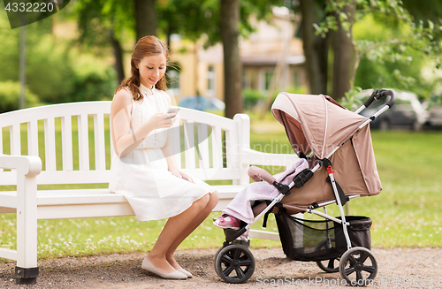 Image of happy mother with smartphone and stroller at park