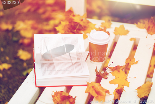 Image of open book and coffee cup on bench in autumn park