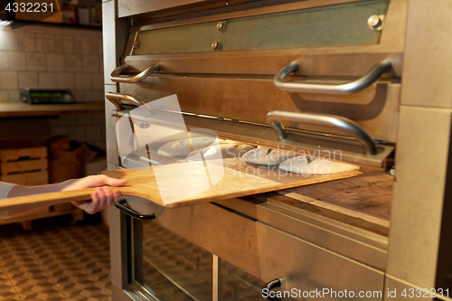 Image of baker hand putting dough into bread oven at bakery