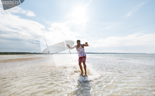 Image of young man riding on skimboard on summer beach