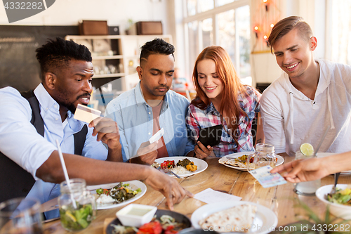 Image of happy friends with money paying bill at restaurant