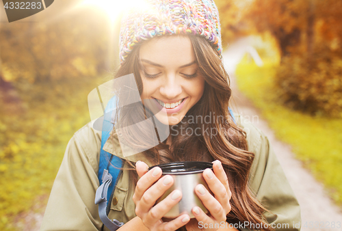 Image of smiling young woman with cup and backpack hiking