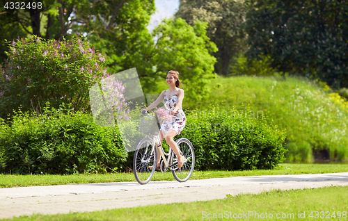 Image of happy woman riding fixie bicycle in summer park