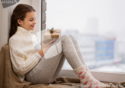 Image of girl with christmas gift sitting on sill at home