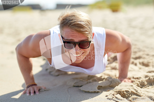 Image of smiling young man doing push-ups on summer beach