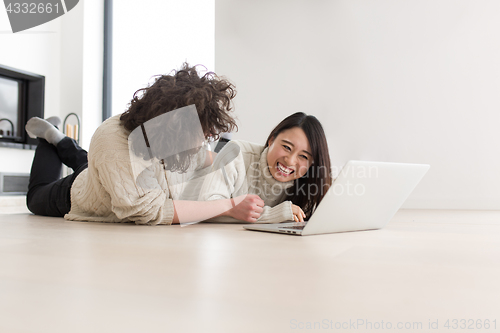 Image of young multiethnic couple using a laptop on the floor