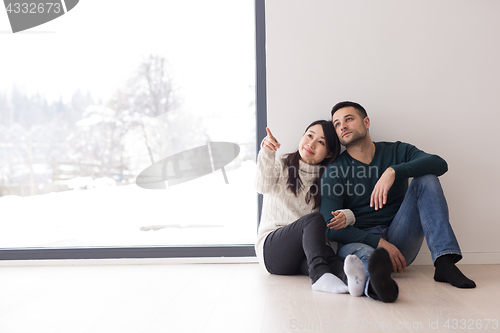 Image of multiethnic couple sitting on the floor near window at home