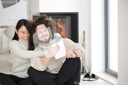 Image of multiethnic couple using tablet computer in front of fireplace