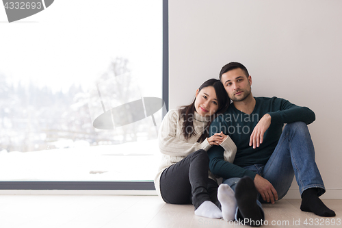 Image of multiethnic couple sitting on the floor near window at home