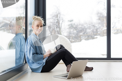 Image of woman drinking coffee and using laptop at home