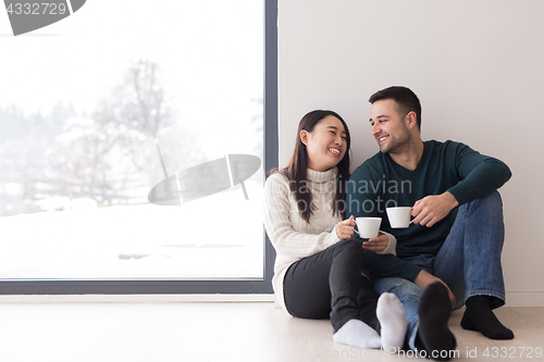 Image of multiethnic couple enjoying morning coffee by the window