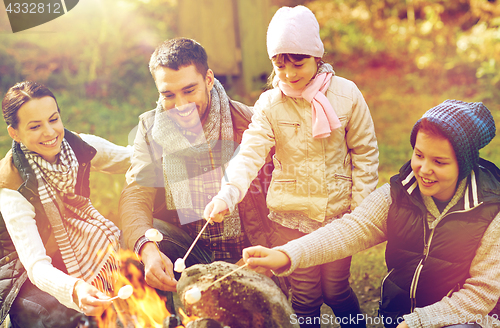 Image of happy family roasting marshmallow over campfire