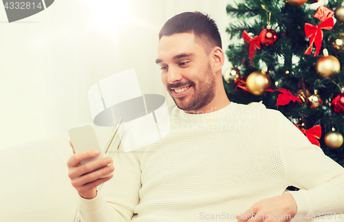 Image of smiling man with smartphone at home for christmas