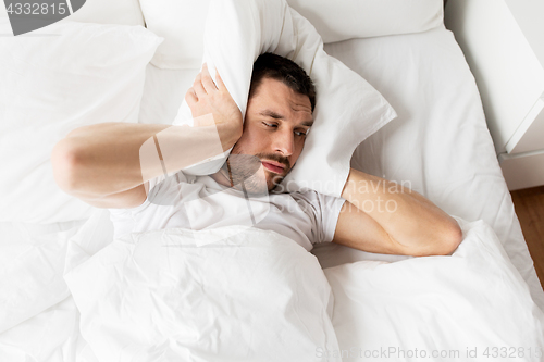 Image of man in bed with pillow suffering from noise