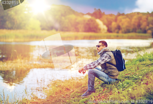 Image of man with backpack resting on river bank