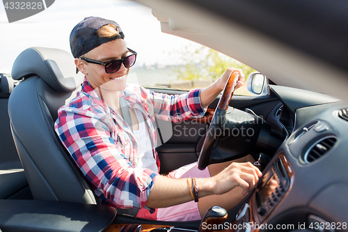 Image of happy young man driving convertible car