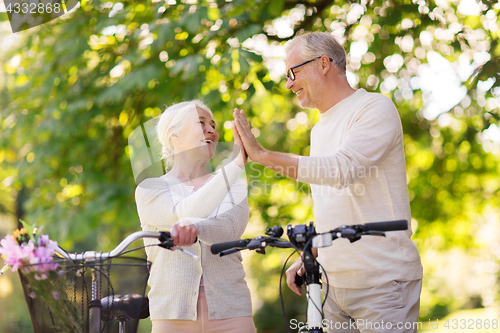 Image of senior couple with bikes making high five at park