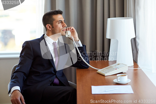 Image of businessman calling on desk phone at hotel room