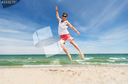 Image of smiling young man jumping on summer beach